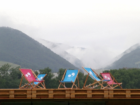 Liegestühle im Vordergrund, im Hintergrund Berge im Nebel. 